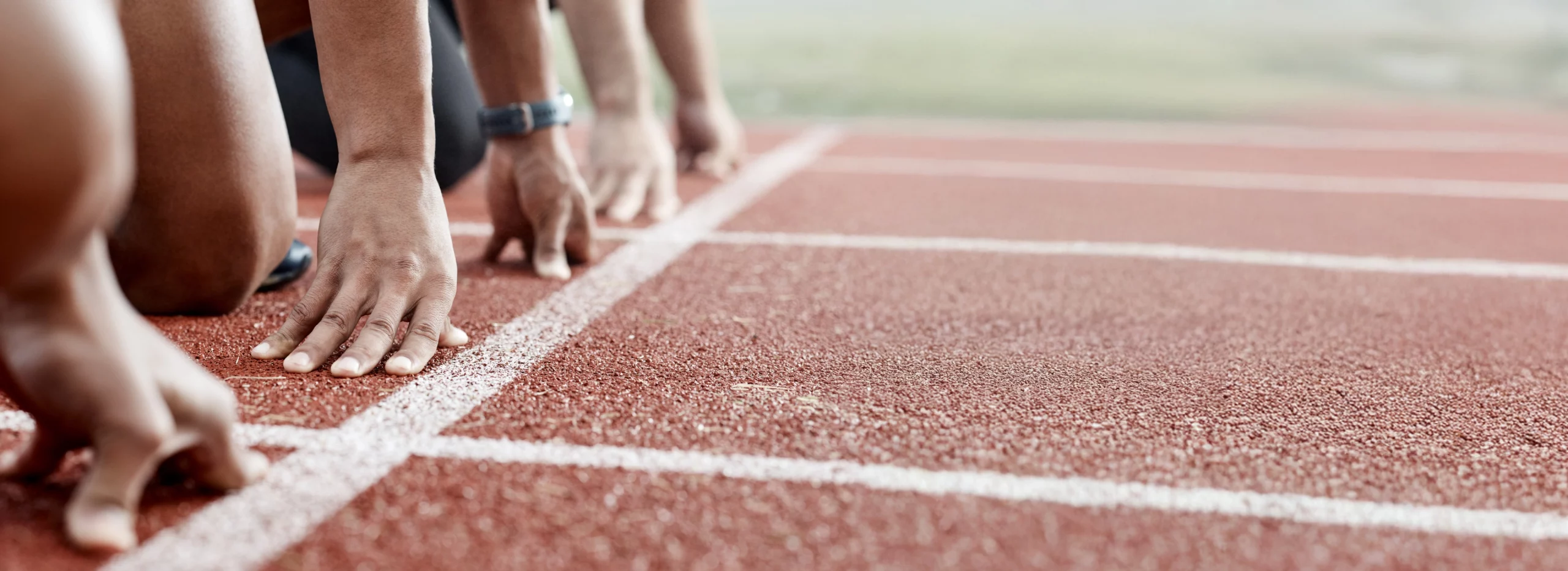 Un départ de course de sprint, les mains sont posées près de la ligne, les coureurs sont prêts à sprinter.