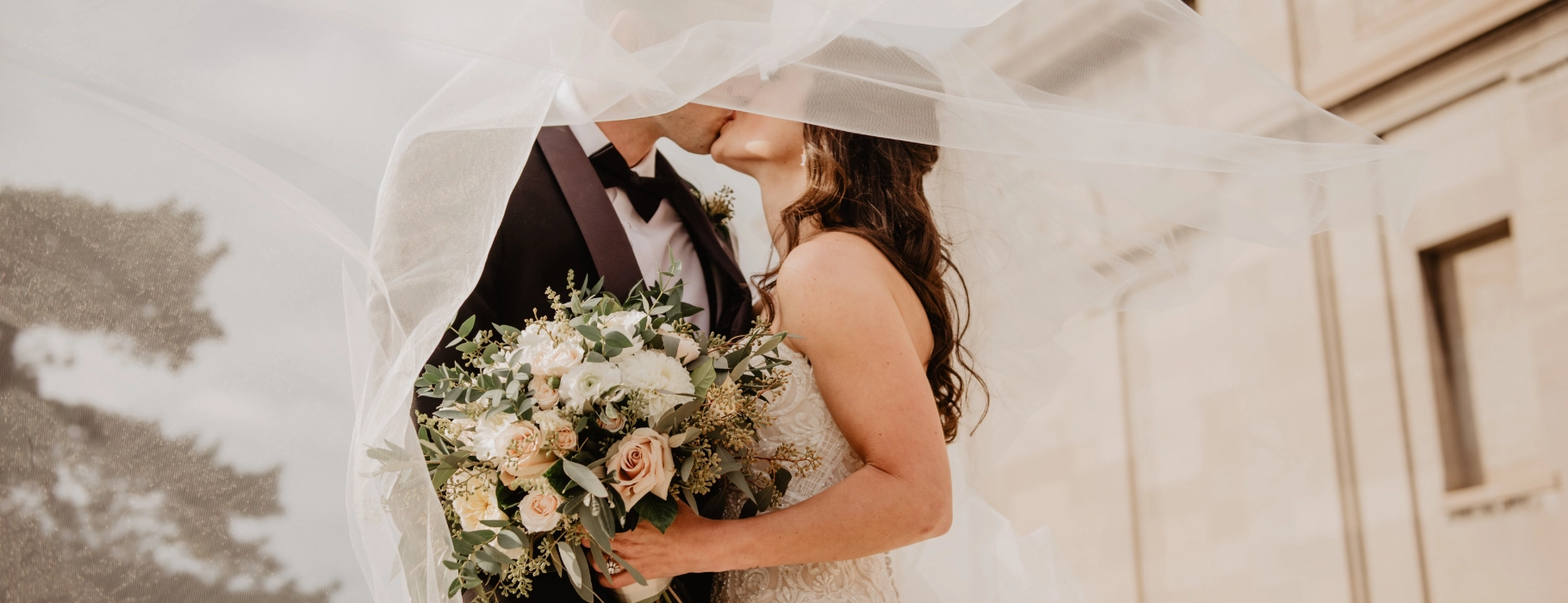 Ein frisch verheiratetes Paar, das sich unter dem Schleier küsst